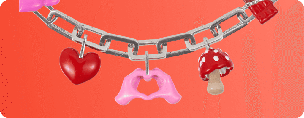 Silver chain bracelet with colorful charms including a red heart, pink hands forming a heart, and a red mushroom.