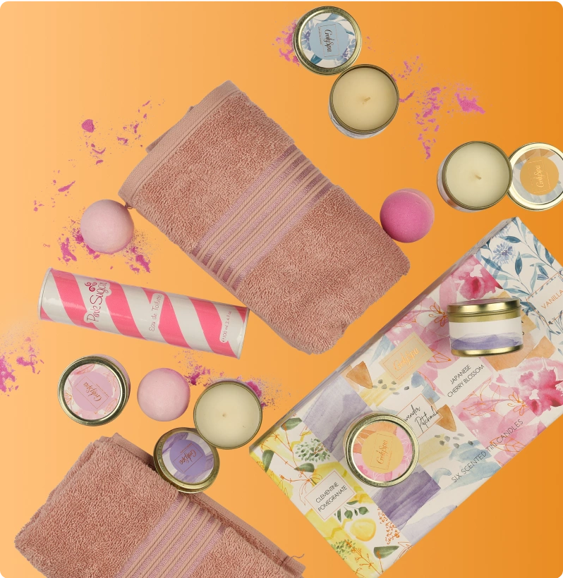 Flat lay of spa and self-care items including pink towels, scented candles, bath bombs, and floral gift packaging on an orange background.