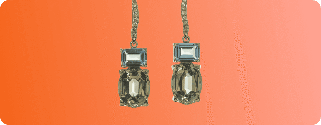 Elegant gold drop earrings with rectangular blue gemstones and oval green gemstones on red background.