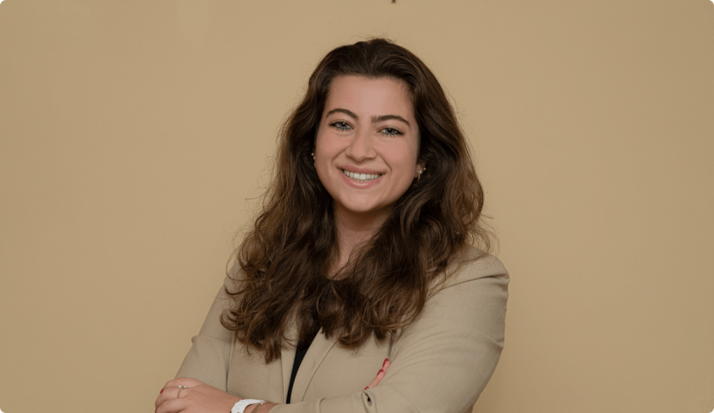 Smiling woman with long brown hair in a beige blazer posing confidently against a plain background.