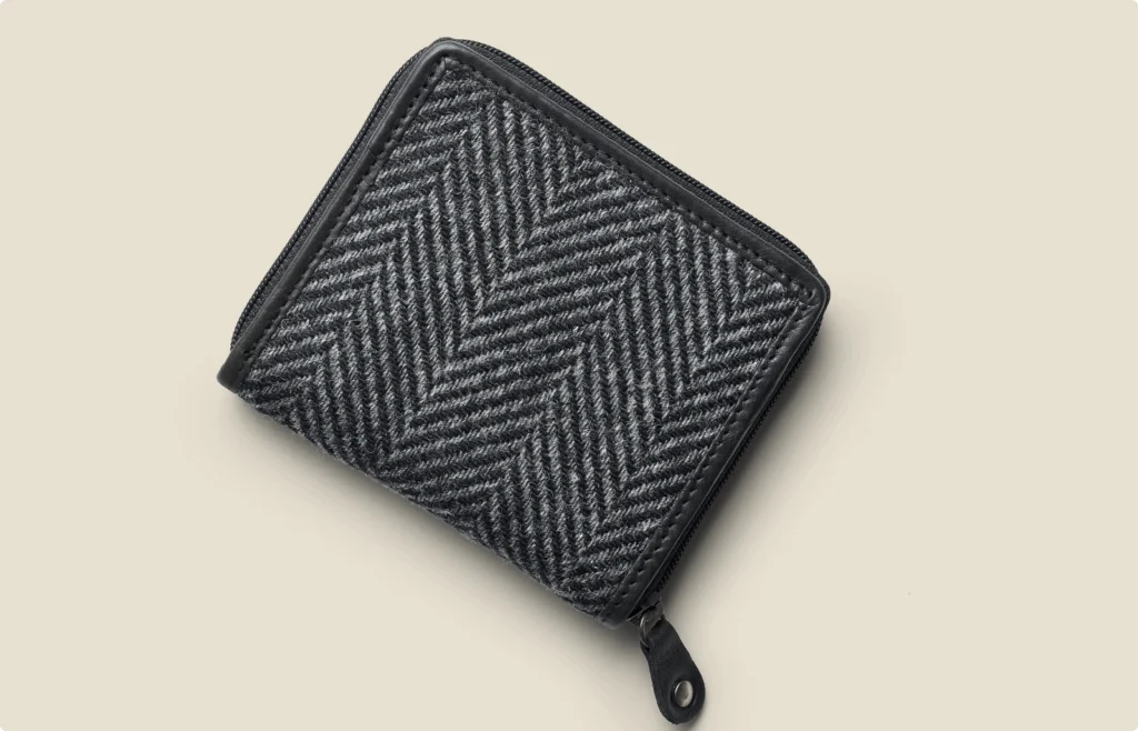 Gray herringbone-patterned zip wallet with black trim on a light beige background.