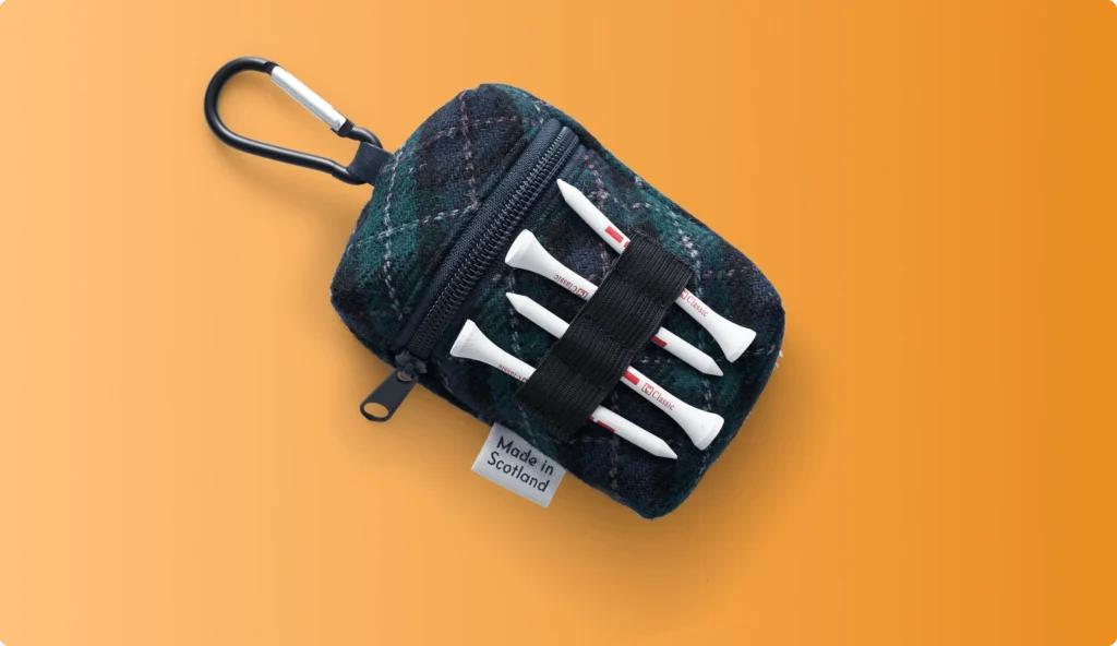 Tartan-patterned golf accessory pouch with white tees attached on an orange background.