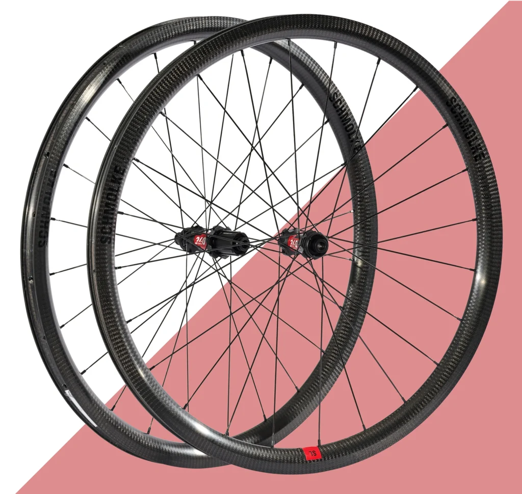 Pair of carbon fiber bicycle wheels with black spokes and red hubs on geometric background.