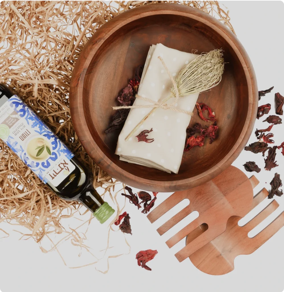 Wooden bowl with napkin, olive oil bottle, wooden utensils, and dried flowers arranged on a white background