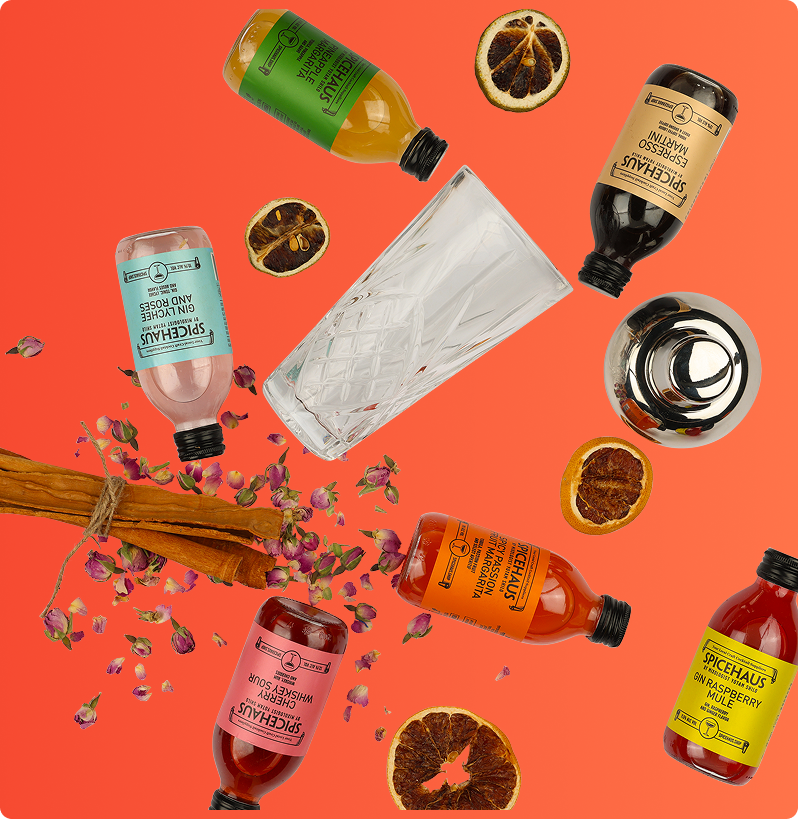 Assorted cocktail mix bottles with glass, shaker, cinnamon sticks, and dried fruit on an orange background