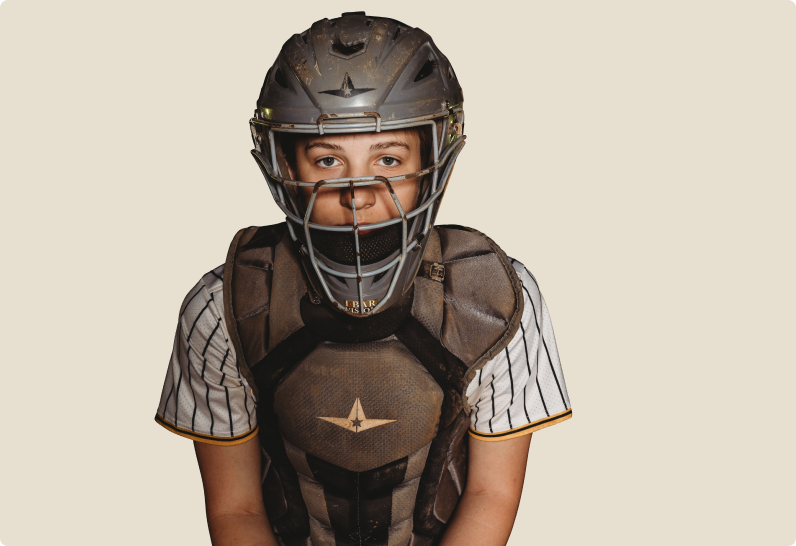 Young baseball catcher in striped uniform wearing helmet and chest protector against a plain background."